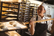 © Wavebreak Media - Asian female mid adult baker keeping bun dough baking tray with long spatula in rack