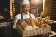 © Wavebreak Media - Smiling asian mid adult female baker looking at fresh breads in basket while standing in bakery