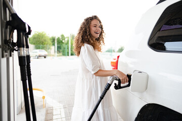 Young curly woman refueling car at gas station