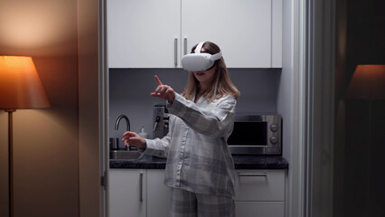 Poster - Young woman in pajamas put on virtual reality headset standing in kitchen