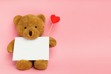 Cute teddy bear with red heart and blank card on pink background, space for text. Valentine's day celebration