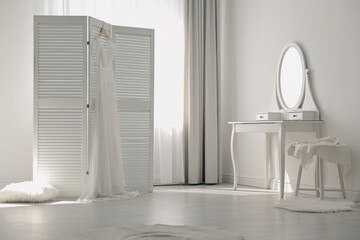 Beautiful wedding dress hanging on folding screen in room