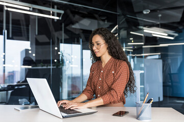 Beautiful indian woman programmer web developer focused and confident working on laptop writing code programming business woman worker in modern office working in casual clothes.