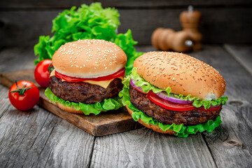 Wall Mural - Two delicious homemade burgers of beef on an old wooden table. Fat unhealthy food close-up.