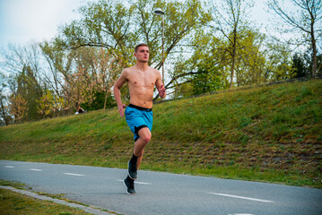 Wall Mural - Good looking young Hispanic guy jogging at a park on a sunny day and smiling