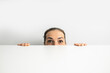 Young woman peeking out from behind white cardboard on white background