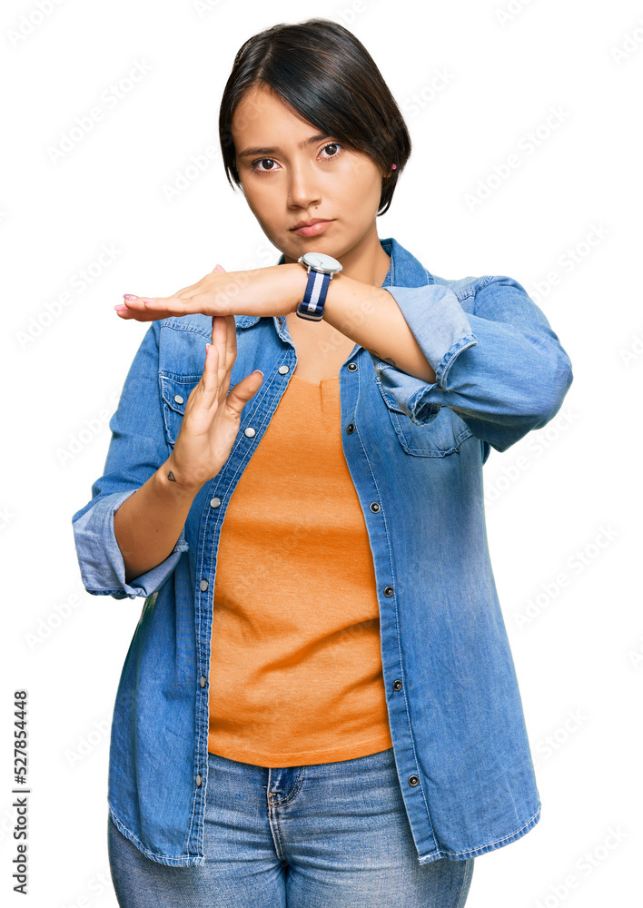 Young beautiful hispanic woman with short hair wearing casual denim jacket doing time out gesture with hands, frustrated and serious face