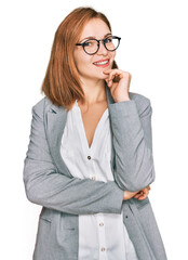 Wall Mural - Young caucasian woman wearing business style and glasses looking confident at the camera smiling with crossed arms and hand raised on chin. thinking positive.