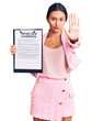 © Krakenimages.com - Young beautiful latin girl holding clipboard with terms and conditions document with open hand doing stop sign with serious and confident expression, defense gesture