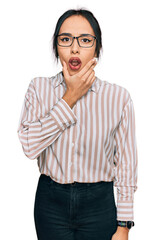 Wall Mural - Young hispanic girl wearing casual clothes and glasses looking fascinated with disbelief, surprise and amazed expression with hands on chin