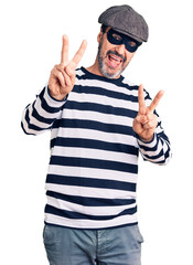 Sticker - Middle age handsome man wearing burglar mask smiling looking to the camera showing fingers doing victory sign. number two.