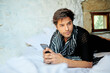 © ADDICTIVE STOCK - Stylish Hispanic man chatting on smartphone on bed