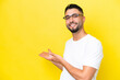 Young Arab handsome man isolated on yellow background With glasses and presenting something