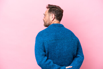 Middle age caucasian man isolated on pink background in back position and looking back