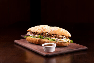 fast food beef brisket sandwich with arugula and coleslaw salad on baguette bread on wooden board wi