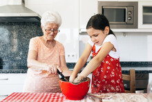 Grandmother With Granddaughter Preparing Dough For Cake In Kitchen
