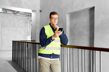 Wall Mural - architecture, construction business and building concept - male supervisor in safety west with smartphone at office