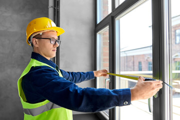 construction business and building concept - male builder with ruler measuring window