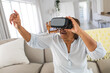 © wavebreak3 - Happy african american senior woman pointing while wearing virtual reality simulator at home