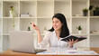 © Prathankarnpap - Smiling asian businesswoman holding notebook and reading information on laptop
