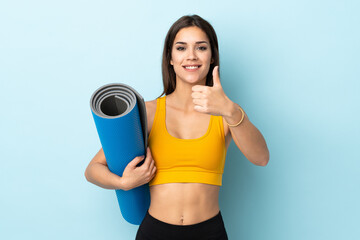 Wall Mural - Young sport woman with mat isolated on blue background with thumbs up because something good has happened