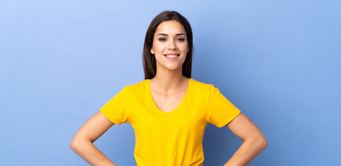 Wall Mural - Young caucasian woman over isolated background posing with arms at hip and smiling