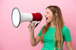 © luismolinero - Young blonde woman isolated on pink background shouting through a megaphone to announce something in lateral position