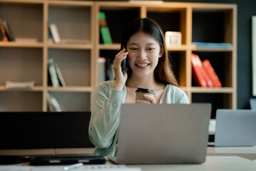 Wall Mural - Beautiful Asian woman talking on the phone in the office of a startup company, she is a company finance employee working in the finance department. Concept of women working in a company.