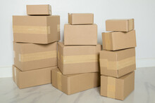 Stack Of Cardboard Boxes For Moving, Empty Room With A White Wall And Cardboard Boxes With Unbranded Barcode On The Floor. Delivery Of Goods, Shopping. Cardboard Boxes On Gray Wall Background.