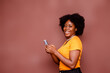 Happy excited African American lady on Afro hair style using mobile phone at studio standing behind a blank background