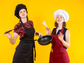 Women in chef's hats. Housewife girls prepare food. Women cooks hold frying pans. Concept of learning cooking. Chefs amateurs on yellow. 