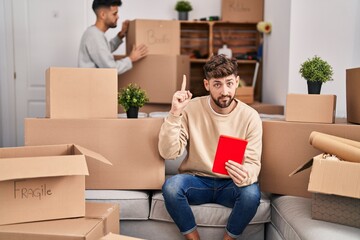 Wall Mural - Homosexual couple moving to a new home smiling with an idea or question pointing finger with happy face, number one