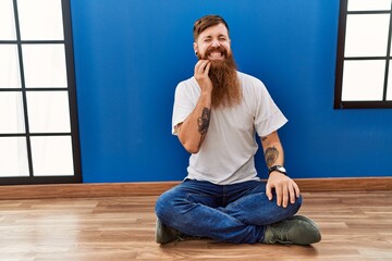 Sticker - Redhead man with long beard sitting on the floor at empty room touching mouth with hand with painful expression because of toothache or dental illness on teeth. dentist