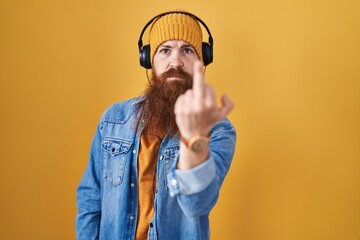 Canvas Print - Caucasian man with long beard listening to music using headphones showing middle finger, impolite and rude fuck off expression