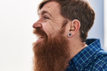 Sticker - Young redhead man using deafness aid machine sitting on sofa at home