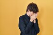 © Krakenimages.com - Young man wearing glasses over yellow background with sad expression covering face with hands while crying. depression concept.