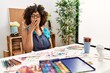 Beautiful african american woman with afro hair painting at art studio bored yawning tired covering mouth with hand. restless and sleepiness.