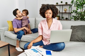 Sticker - Mother of interracial family working using computer laptop at home puffing cheeks with funny face. mouth inflated with air, crazy expression.