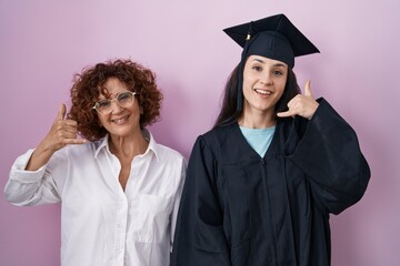 Sticker - Hispanic mother and daughter wearing graduation cap and ceremony robe smiling doing phone gesture with hand and fingers like talking on the telephone. communicating concepts.