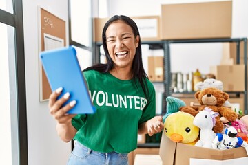 Poster - Young latin woman wearing volunteer uniform having video call at charity center