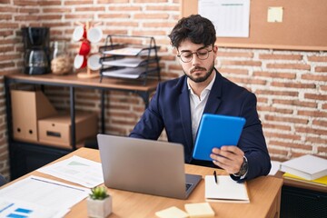 Wall Mural - Young hispanic man business worker using laptop and touchpad at office