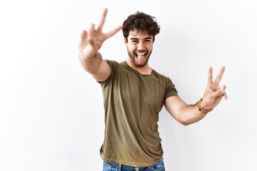 Canvas Print - Hispanic man standing over isolated white background smiling with tongue out showing fingers of both hands doing victory sign. number two.