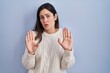 © Krakenimages.com - Young brunette woman standing over blue background moving away hands palms showing refusal and denial with afraid and disgusting expression. stop and forbidden.