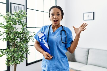 Wall Mural - Young african american woman working wearing doctor uniform working at the clinic celebrating victory with happy smile and winner expression with raised hands