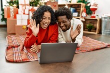 Young Interracial Couple Having Video Call Using Laptop Lying On The Floor By Christmas Tree At Home.