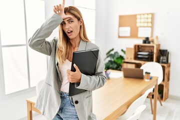 Poster - Blonde business woman at the office making fun of people with fingers on forehead doing loser gesture mocking and insulting.