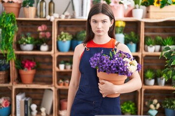 Sticker - Young caucasian woman working at florist shop holding pot with flowers thinking attitude and sober expression looking self confident