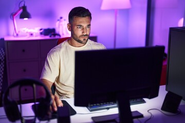 Canvas Print - Young hispanic man streamer sitting on table with serious expression at gaming room