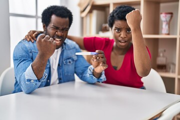 Sticker - Young african american couple holding pregnancy test result annoyed and frustrated shouting with anger, yelling crazy with anger and hand raised