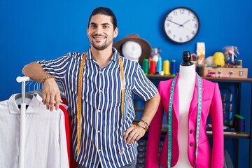 Sticker - Young hispanic man tailor smiling confident leaning on clothes rack at sewing studio